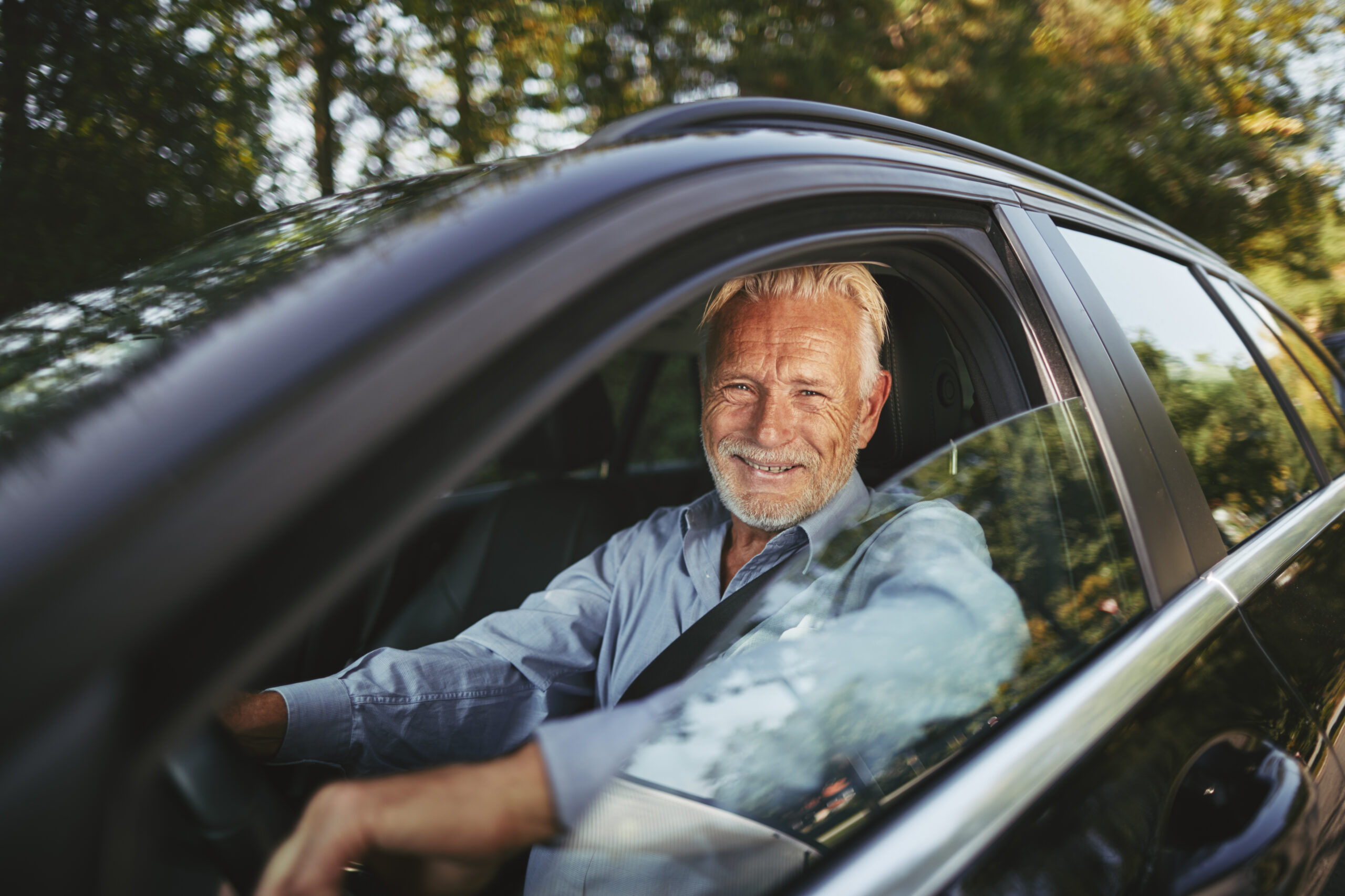 Smiling senior man driving along a road in the countryside